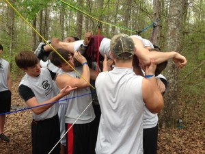 Members of the Quarterback Club help one another through a ropes course.